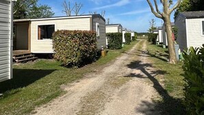 A row of mobile homes with a gravel path between them, surrounded by greenery and trees. - ZEcamping familial avec piscine - proche Oléron (La Tremblade)