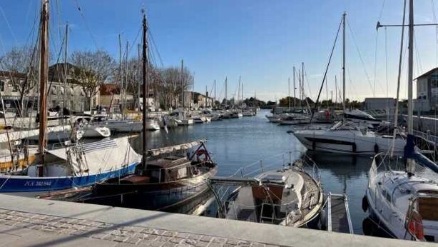 A marina with multiple boats docked along a calm waterway, surrounded by buildings. - ZEcamping familial avec piscine - proche Oléron (La Tremblade)