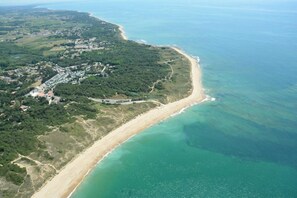 An aerial view of a coastal area with a sandy beach, dense greenery, and a small settlement with buildings.