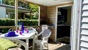 A covered outdoor area with a table and chairs, a small garden, and a door leading to a kitchen. - ZEcamping 5 étoiles pet friendly animé avec piscine couverte en bord de mer (Saint-Georges-d'Oléron)