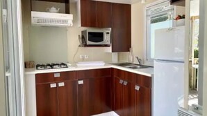 A compact kitchen with dark wooden cabinets, a white countertop, a microwave, a gas stove, and a refrigerator. - ZEcamping 5 étoiles pet friendly animé avec piscine couverte en bord de mer (Saint-Georges-d'Oléron)