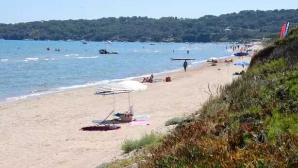 Une plage avec un rivage sablonneux, quelques parasols et quelques personnes.