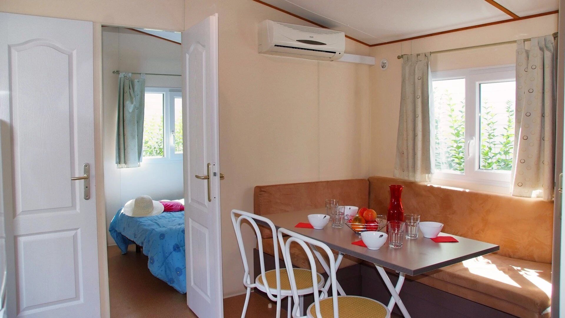 A room with a bed, a table with chairs, a window with curtains, and an air conditioning unit.