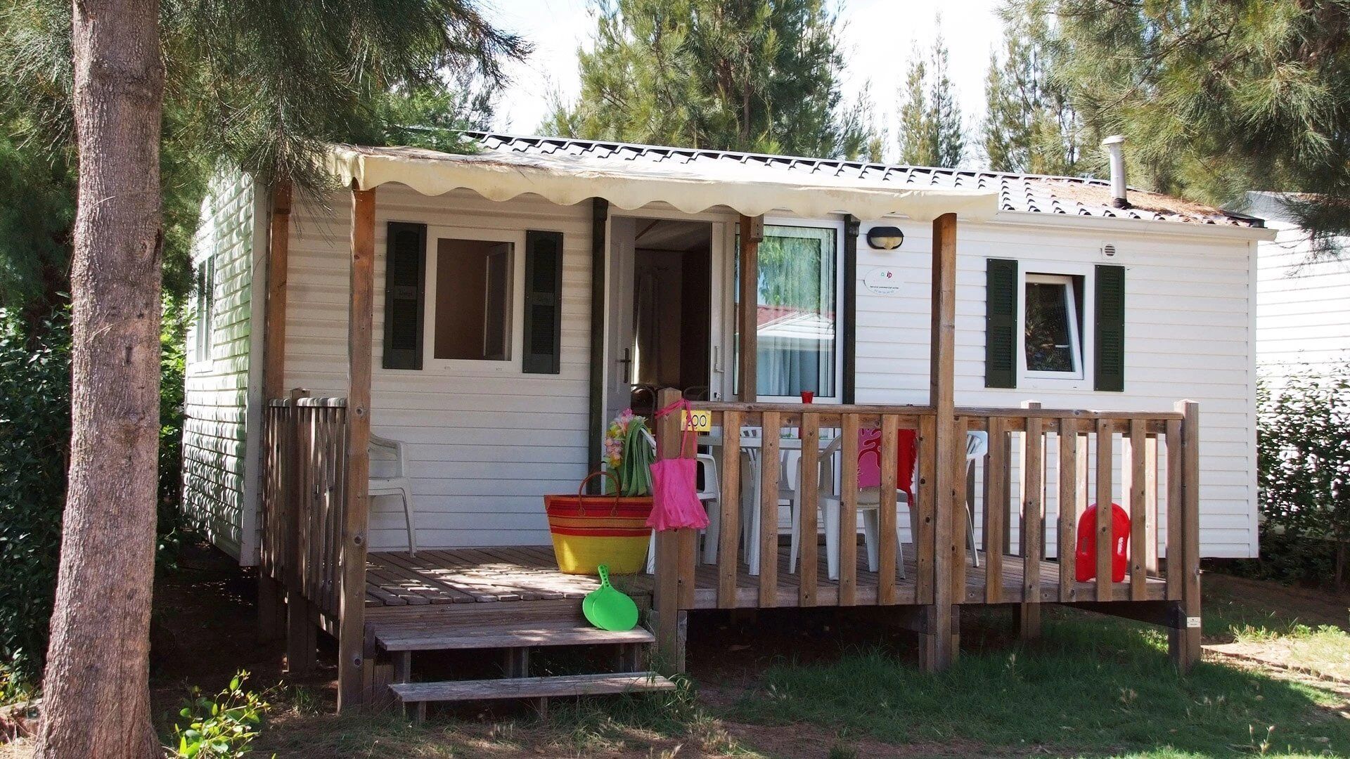 A small, single-story mobile home with a porch, a wooden deck, and a small front yard.