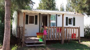 Une petite maison mobile d’un seul étage, dotée d’un porche, d’une terrasse en bois et d’un petit jardin devant.