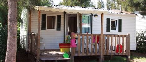 A small, single-story mobile home with a porch, a wooden deck, and a small front yard.