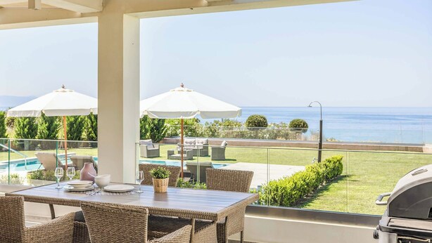Eine Terrasse mit Esstisch, Stühlen und Sonnenschirmen mit Blick auf einen Swimmingpool und das Meer.