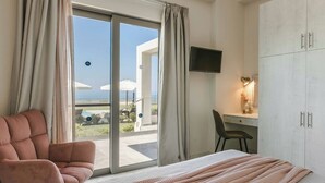 Ein Hotelzimmer mit Bett, Sessel, Schreibtisch, Fernseher und einer Schiebetür zu einem Außenbereich mit Sonnenschirmen.