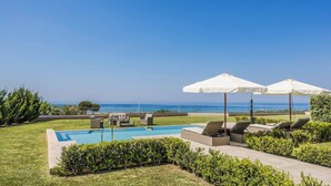 Ein Poolbereich mit Liegestühlen und Sonnenschirmen, mit freiem Blick auf den Ozean und gepflegter Bepflanzung.