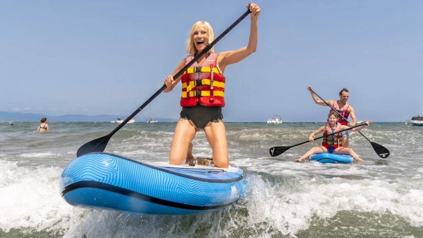Two people on a blue inflatable raft in the ocean, wearing life jackets.