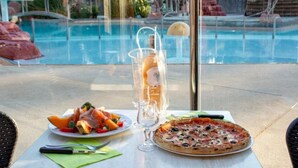 Una mesa con un plato de comida, un vaso de agua y una botella de vino, con vistas a la piscina.