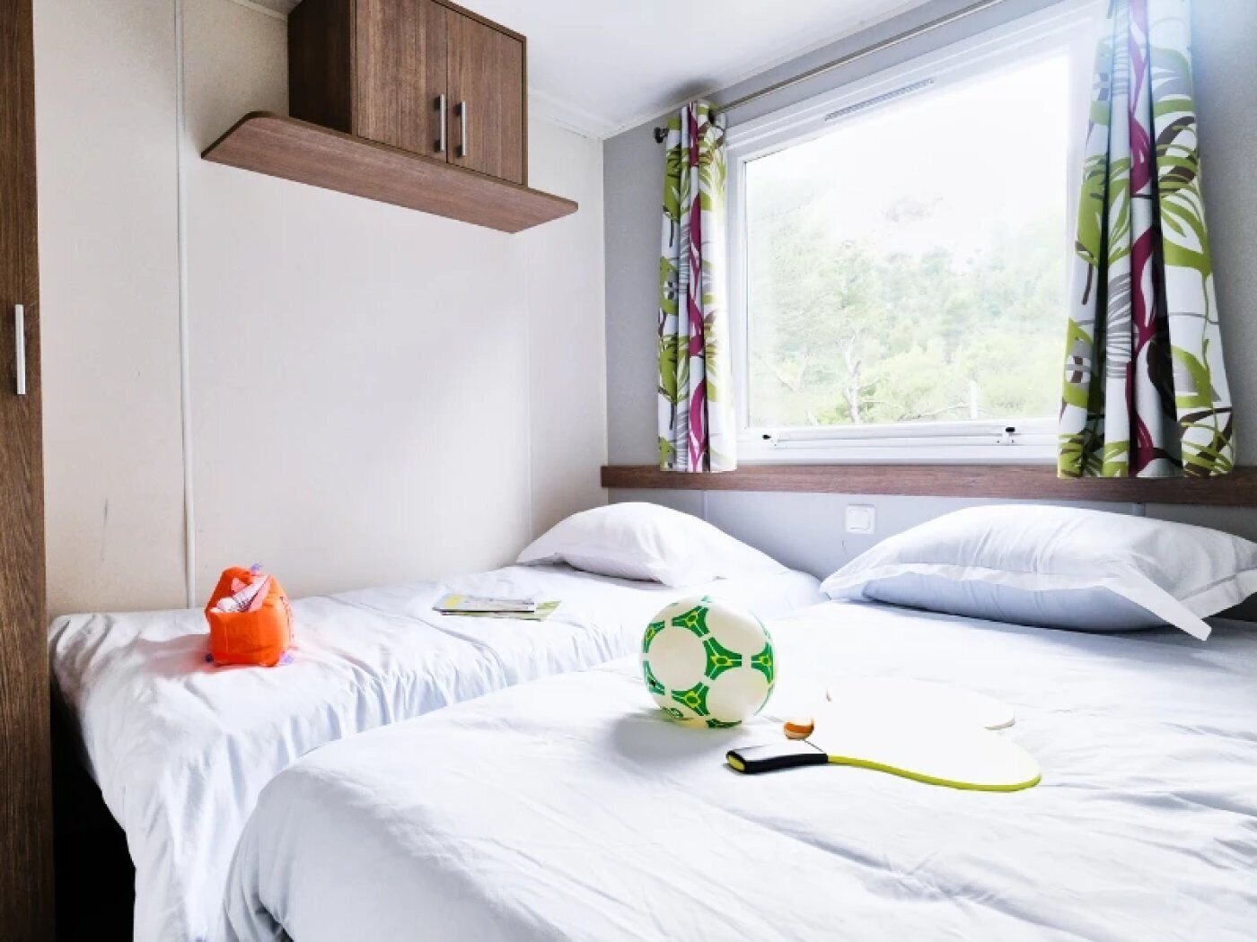 Un dormitorio con cama, almohadas, una ventana con cortinas, un armario de madera y una pelota de fútbol.