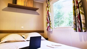 A hotel room with a bed, a laptop, a wooden shelf, and a window with curtains.