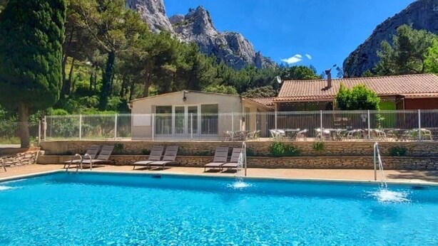 A swimming pool with lounge chairs, a covered seating area, and a view of mountains.