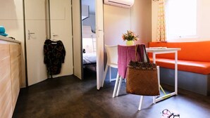 Una habitación compacta con una cama, una mesita con un florero, una silla, un sofá, un armario y un equipo de aire acondicionado.