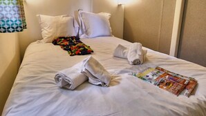 Una cama bien hecha con sábanas blancas, dos toallas enrolladas y una revista sobre la cama.