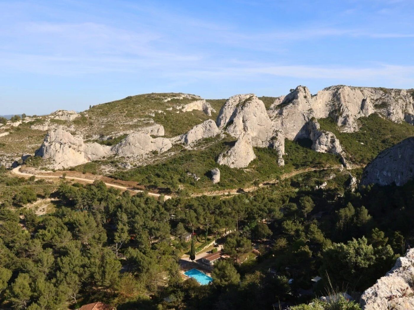 Paisaje montañoso con afloramientos rocosos, bosque denso y una piscina.