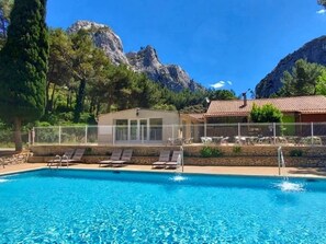 Ein Swimmingpool mit Liegestühlen, einer überdachten Lounge und Blick auf Berge.