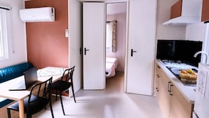 A compact kitchen with a stove, sink, and a dining area with a table and chairs. - ZEcamping 4 étoiles piscine animaux acceptés mobil-home TV LV clim (Orgon)