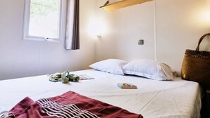 Un dormitorio con cama, ventana con cortinas, estante montado en la pared y una cesta tejida.