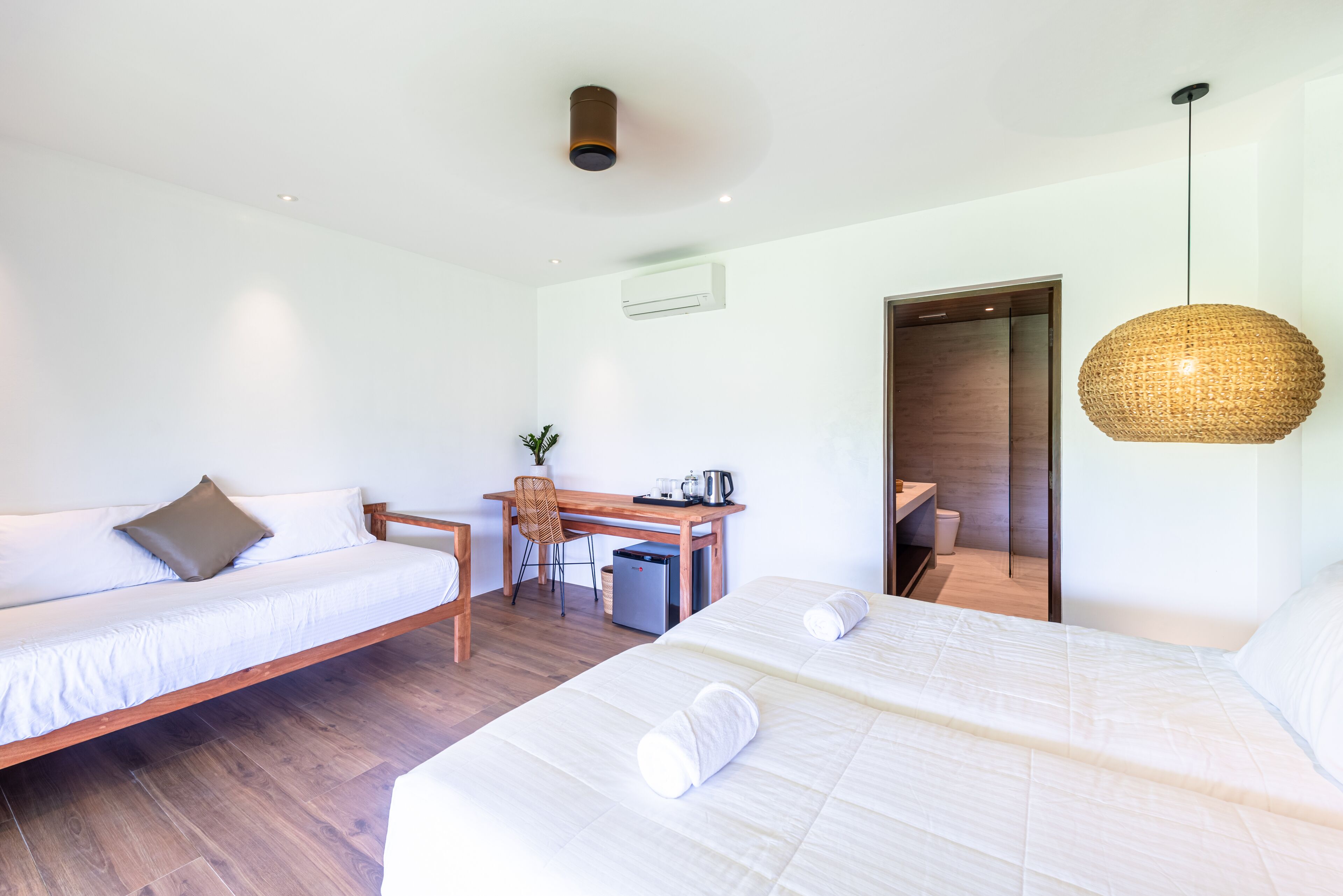 A modern hotel room with two beds, a desk, and a small kitchenette.