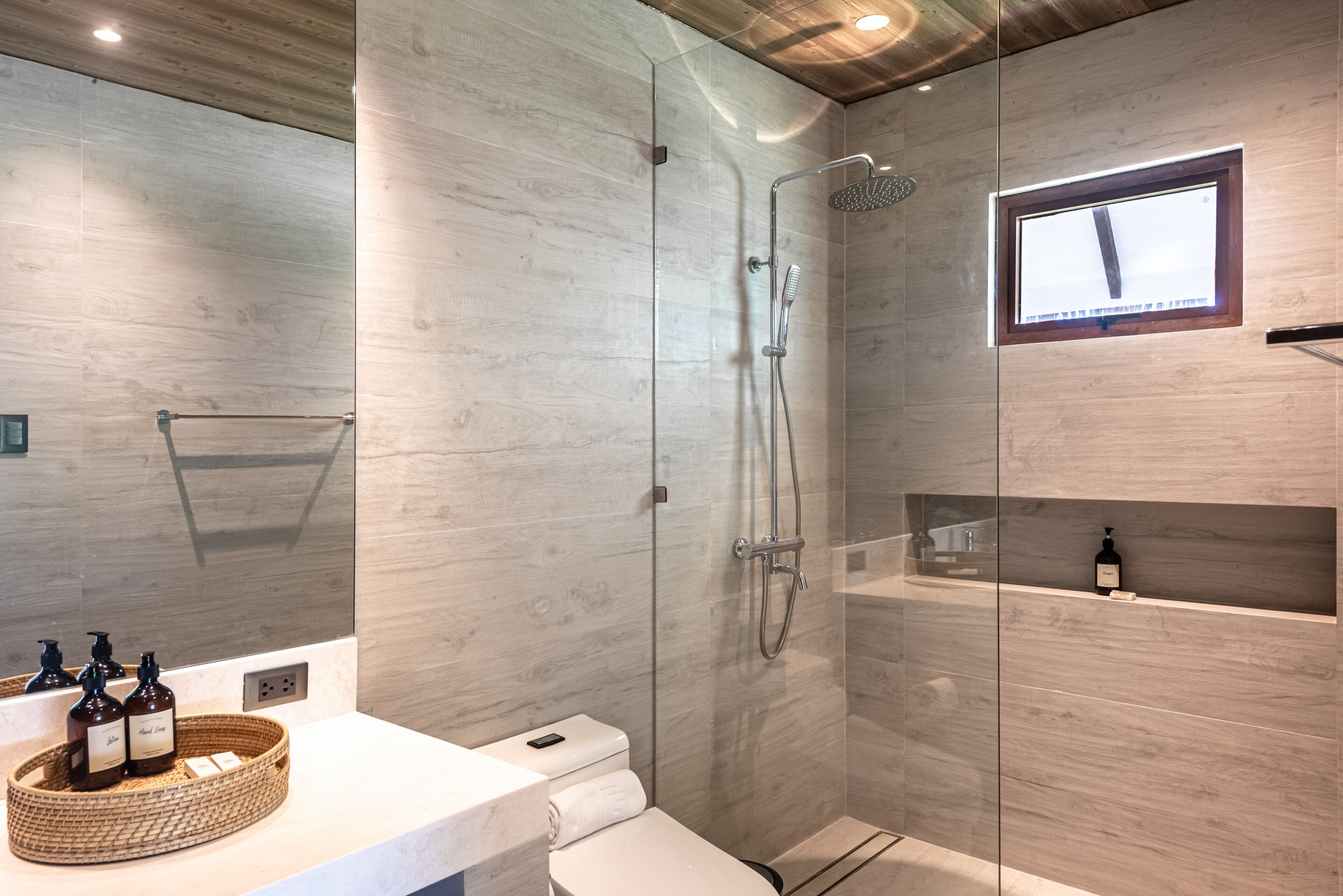 Ein modernes Badezimmer mit einer gläsernen Duschkabine, einem Holzwaschtisch und einer kleinen Ablage mit Toilettenartikeln.