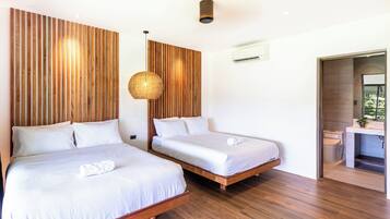 Un dormitorio moderno con dos camas, paneles de madera en las paredes, un colgante de techo y un baño pequeño con lavamanos y espejo.