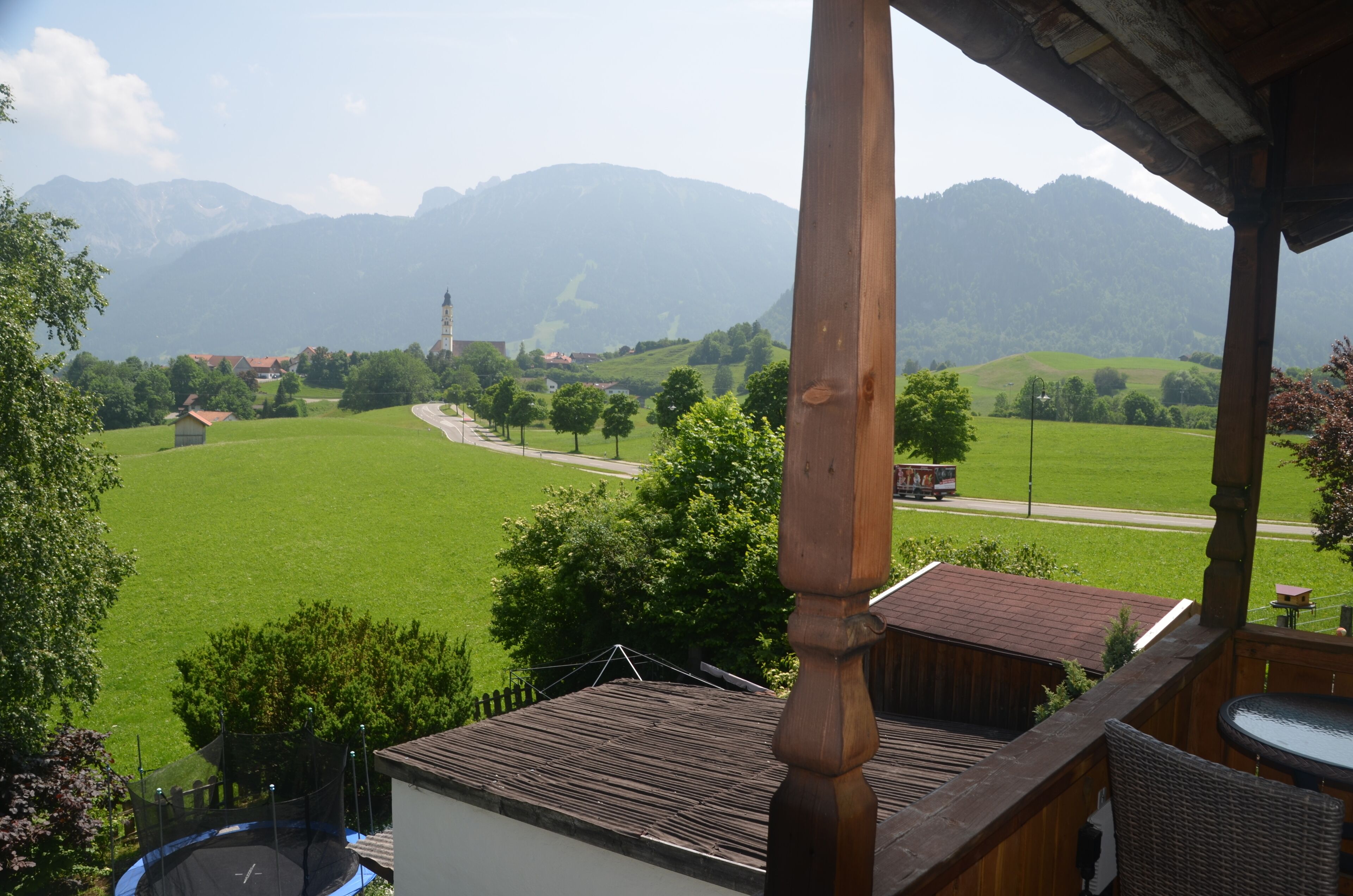 Une vue depuis un balcon donnant sur un champ verdoyant, une église et des montagnes.