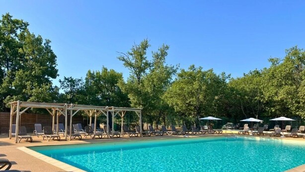 Una piscina con sillas de descanso y sombrillas, rodeada de árboles.