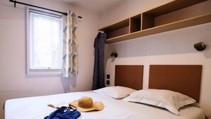 Una cama bien tendida con sábanas blancas, un sombrero de paja y una prenda azul sobre la cama.