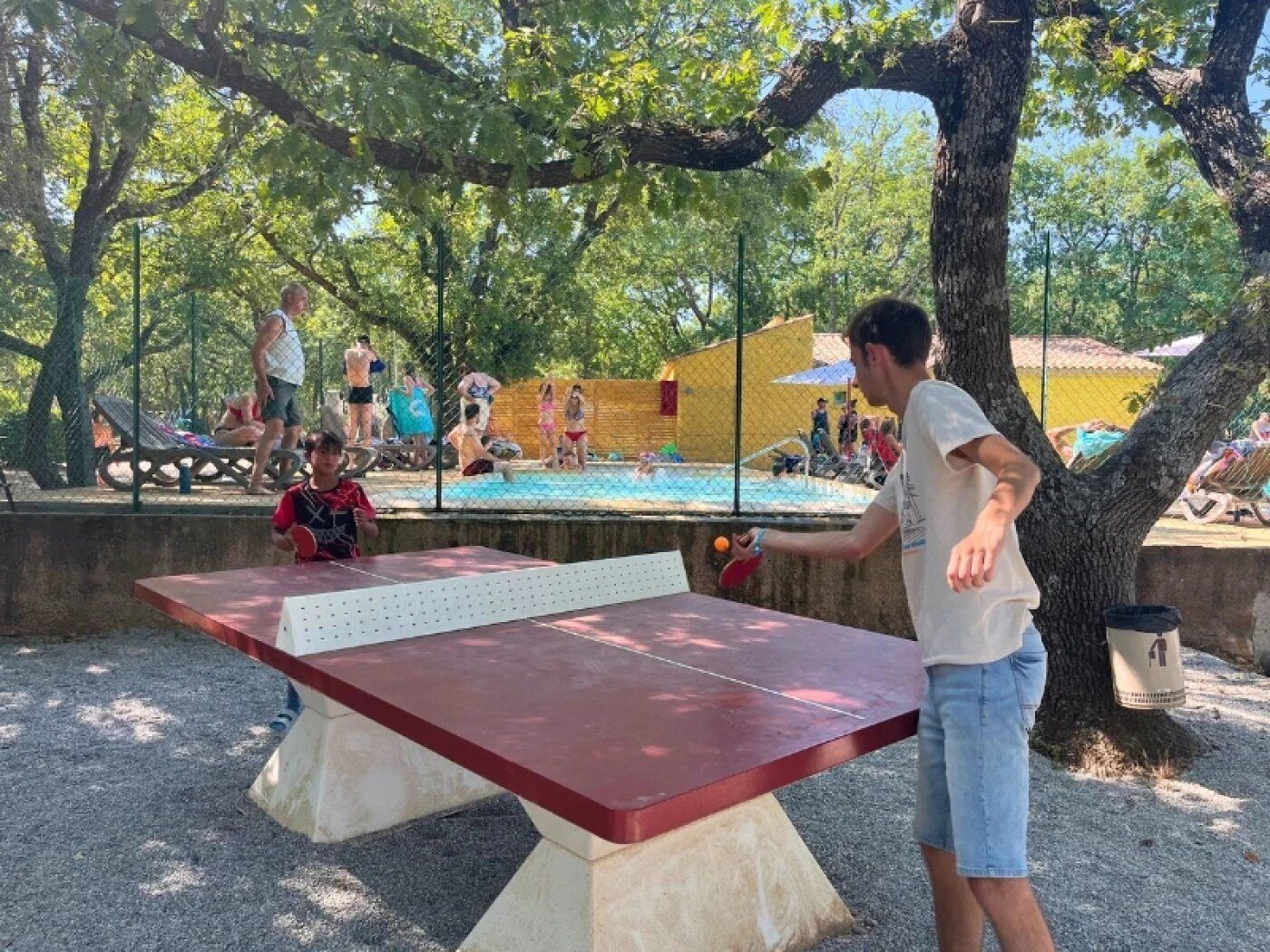A ping pong table in an outdoor area with trees and a pool in the background.