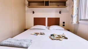 Ein Einzelbett mit Holz-Kopfteil, eine kleine Ablage darüber und ein Fenster mit Vorhängen.