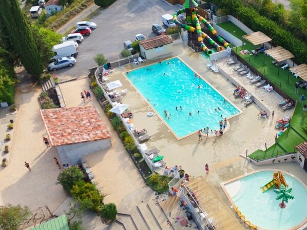 Luftaufnahme eines Poolbereichs mit Wasserrutsche, Liegestühlen und einem kleinen Gebäude.