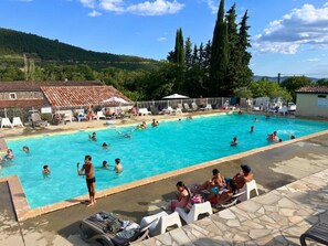 Ein Schwimmbecken mit Schwimmern und Liebespaaren. Liegestühle und Sonnenschirme sind vorhanden.