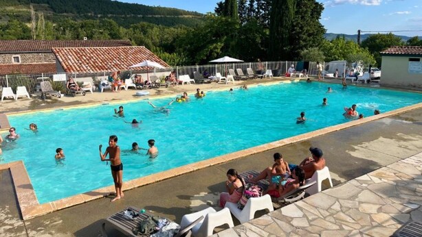 A swimming pool with people swimming and lounging. There are lounge chairs and umbrellas.