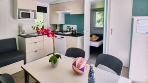 A compact room with a kitchenette, a dining area with a table and chairs, a small bed, and a window with a view of greenery.