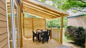 A wooden deck with a table and chairs, a covered area, and a lounge chair with bags.