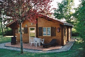 A wooden cabin with a patio, a table, chairs, and a fire extinguisher.