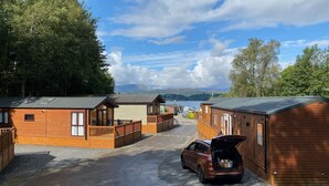 A row of wooden cabins with a gravel driveway and a car parked in front. - V+B's Hygge, Gorgeous Lake View at V&B Hygge (Troutbeck Bridge)