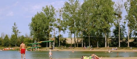 Un parque junto al lago con un área de juegos, zonas de picnic y gente relajándose junto al agua.