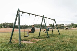 Columpio en un parque con un campo cubierto de césped y árboles al fondo.