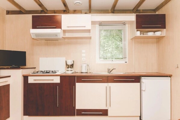 Cocina compacta con armarios de madera, estufa integrada, lavamanos y ventana con persianas.