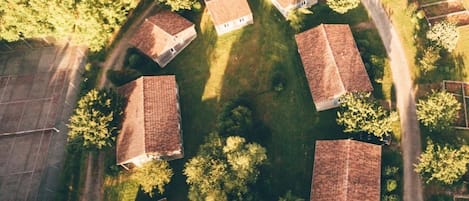 An aerial view of a residential area with houses arranged in a circular pattern, surrounded by trees and a clear sky.