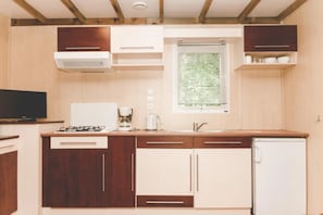 Cocina compacta con armarios de madera, estufa integrada, cafetera y una ventana con persianas.