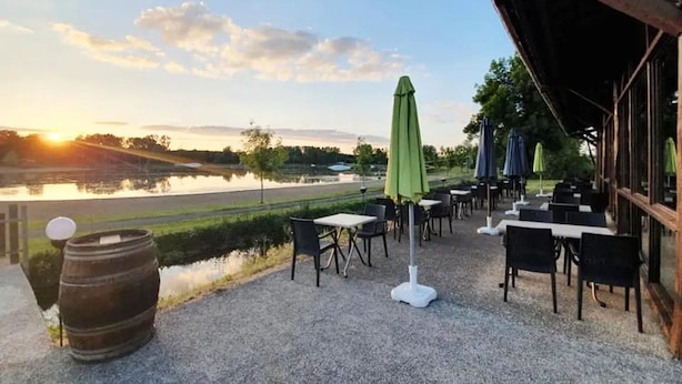 An outdoor patio area with tables and chairs, a view of a lake, and a sunset in the background.