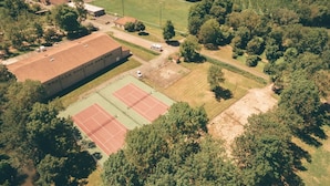 An aerial view of a residential area with a large building, tennis courts, and surrounding greenery.