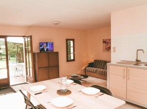 A dining area with a table set for four, a television on a cabinet, and a kitchen with a sink and cabinets.