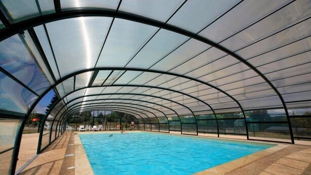 An indoor swimming pool with a curved glass ceiling, surrounded by a sandy floor and clear blue water.