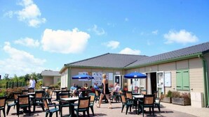 An outdoor cafe with tables and chairs, a building with a tiled roof, and a clear sky.