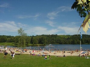Una playa junto al lago, con gente tomando el sol y nadando, rodeada de vegetación.